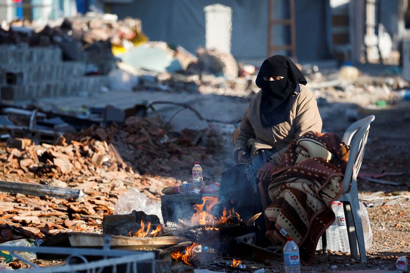 Una persona sentada frente a una hoguera cerca de escombros y restos, tras un terremoto mortal, en Kirikhan, Turquía, 8 de febrero de 2023. REUTERS/Piroschka van de Wouw
